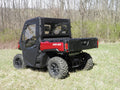 A Can-Am Defender equipped with Offroad Armor Soft Doors and Rear Window Combo is parked on grass near leafless trees, featuring a closed tailgate and large rugged rear tires for off-road use.