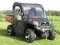 A black and orange CFMOTO UTV with off-road tires features a Cf Moto Uforce 500/800 Soft Full Cab Enclosure With Vinyl Windshield, parked on green grass. It has a front winch, clear vinyl windows, and sits under a bright sky with trees in the background.