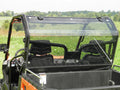 A Cfmoto Uforce 500/800 2pc. Lexan Back Window is installed on an orange utility vehicle in a grassy field, with the window partially open and two black seats inside. Trees and a cloudy sky are visible in the background.