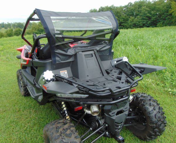 A CFMoto ZForce 950 equipped with a Soft Back Panel is parked on green grass, facing away. The off-road side-by-side features rugged tires, a roll cage with a clear rear window, and is surrounded by lush greenery under cloudy skies.