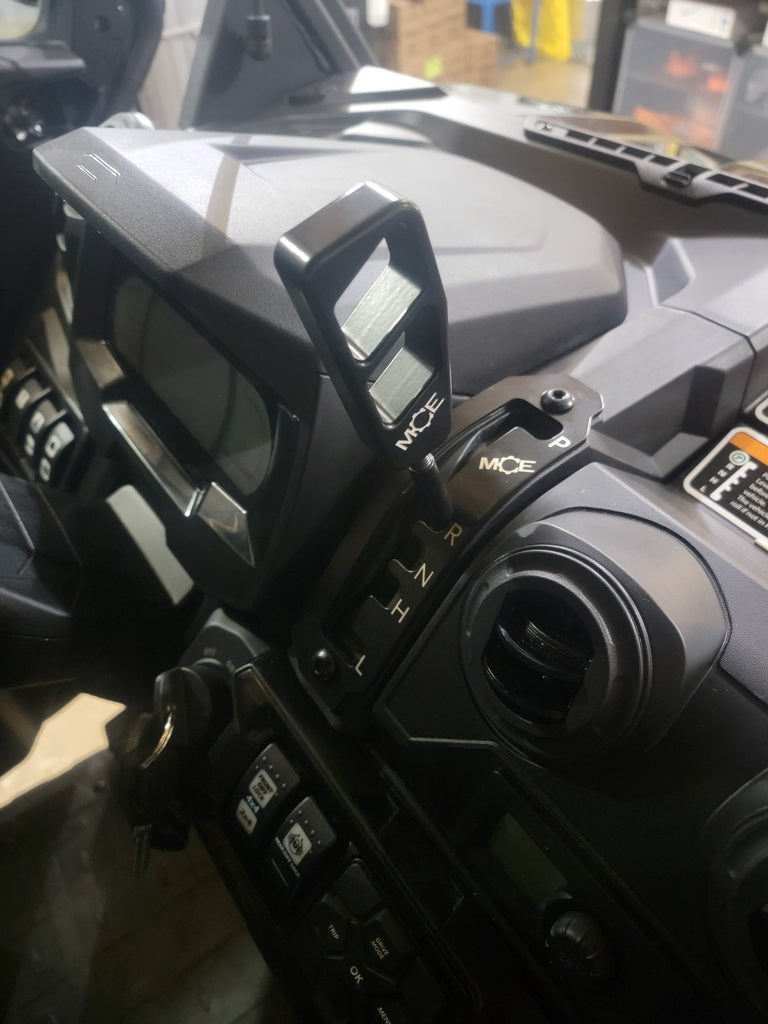 Close-up of a Can-Am Defender HD8, HD9, or HD10 Ultimate Shifter Kit installed on a vehicle dashboard, featuring a gear shifter labeled L, H, N, R with an MCE handle. Surrounding buttons, controls, a vent, and part of the digital display are visible.