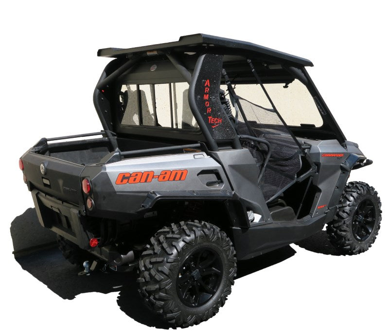 A Canam Commander Glass Rear Window (2011-2019) is installed on a black and gray side-by-side vehicle with rugged tires, a covered roof, rear cargo bed, and red Can-Am branding. The vehicle is pictured on a white background from the back left angle.