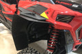 Close-up of a red off-road vehicle with Trail Armor Mud Flap Fender Extensions for the 2018-2019 RZR XP Turbo S. Features include a large mud flap, red coil suspension, rugged tire, and black-yellow geometric decals on angular panels.