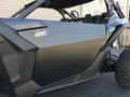 Close-up of a Canam Maverick X3 featuring Dirt Specialties Flat Top Style Half Doors, showing the door panel with Maverick X3 decals, plus part of the front wheel and suspension while parked on pavement.