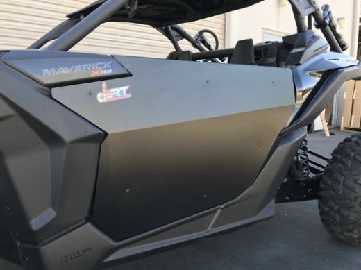 Close-up of a Canam Maverick X3 featuring Dirt Specialties Flat Top Style Half Doors, showing the door panel with Maverick X3 decals, plus part of the front wheel and suspension while parked on pavement.