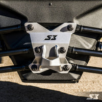 Close-up of the S3 Power Sports 2017+ Can-Am Maverick X3 HD Pull Plate, a silver metal bracket with the S3 logo and star, secured by six black bolts to a black frame—part of an off-road vehicle’s suspension system on concrete.