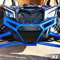 Close-up of a Can-Am Maverick X3 featuring the S3 Power Sports 2017+ Front Bumper with angular black and blue accents, LED headlights, mesh grille, visible suspension, and SX logo, parked on concrete near a brick building.