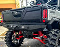 A close-up shows the Can-Am Defender Rear Winch Bumper with Lights, featuring red springs, rugged black tires, a custom black bumper with integrated lights and winch. The tailgate and Can-Am branding are clearly visible.