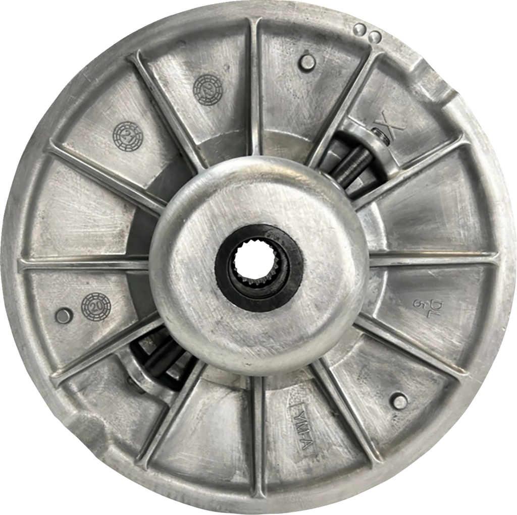 A close-up of a round, metallic mechanical part with radial supports, a central hole containing gear teeth, and engraved markings. The surface shows a matte finish and features various symbols and numbers, suggesting it’s a component of a machine or vehic