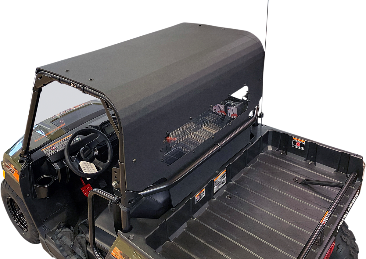 A black utility vehicle with a hard, matte-finish roof covers the cabin and extends over the cargo bed. The bed is empty and ribbed for grip. The cabin has a steering wheel and visible dashboard controls. The background is plain and light-colored.