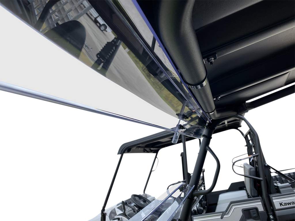 Close-up view of a clear windshield attached to a black metal frame on a rugged, open-sided off-road vehicle. The perspective looks upward, highlighting structural details and outdoor elements in the blurred background.