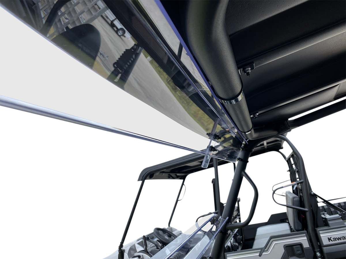 Close-up view of a clear windshield attached to a black metal frame on a rugged, open-sided off-road vehicle. The perspective looks upward, highlighting structural details and outdoor elements in the blurred background.