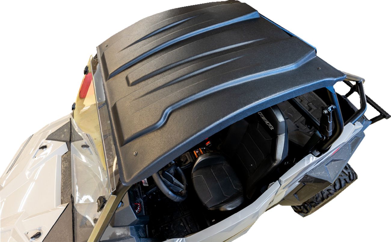 A top-down view of a black UTV roof installed on a white off-road vehicle. The roof has contoured ridges, and the interior shows a black seat, steering wheel, and some dashboard controls. The background is plain and white.