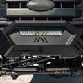 Close-up of the 2011-2016 Ford F-250 Spartan Front Bumper by Road Armor. This textured black, sheet metal pre-runner guard features a center logo, built-in LED light bar, angular lines, and visible suspension and tire components.