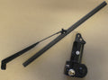 The Cab Windshield Wiper – Pro FXT, featuring a black wiper arm with blade, is displayed beside a compact electric motor with a mounting bracket and metallic connector on a plain brown surface.