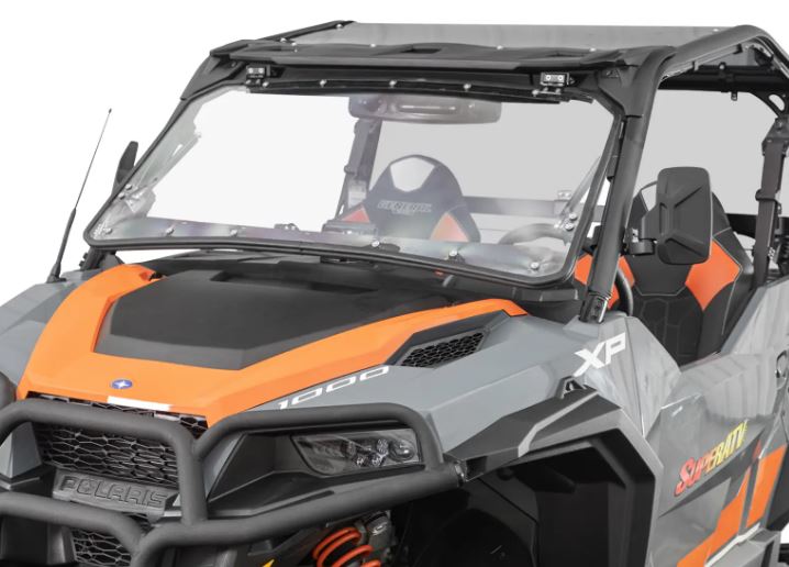 A close-up of a Polaris off-road vehicle features the General Scratch Resistant Flip Down Windshield, off-road tires, side mirrors, and two black seats. The vehicle is gray and orange with XP and 1000 markings visible.