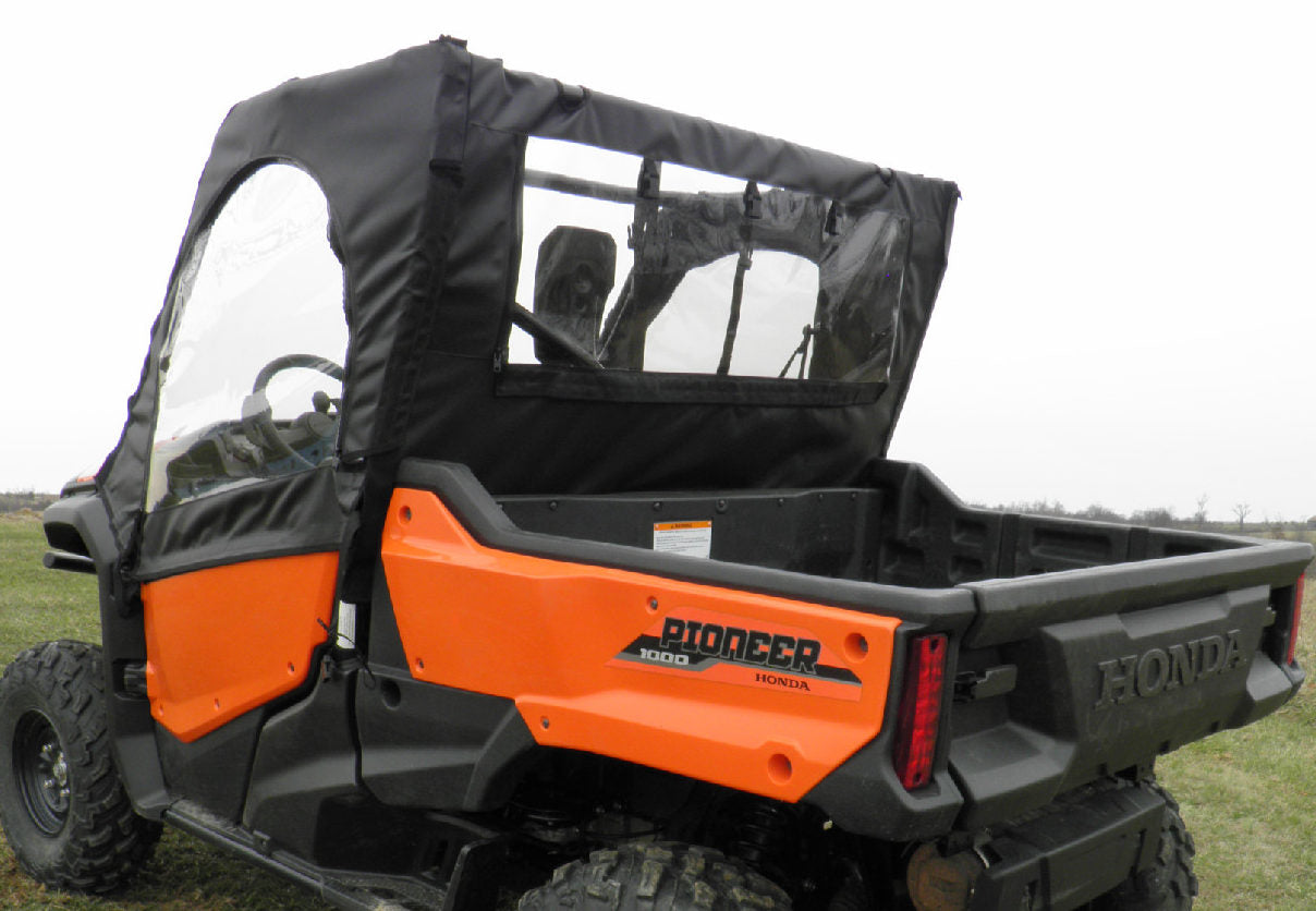 A Honda Pioneer 700 (2014+) with a Soft Door and Rear Window Combo for an existing hard windshield and top is parked on grass, featuring black fabric doors with clear plastic windows, an empty cargo bed, and a cloudy sky in the background.