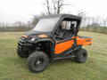 A Honda Pioneer 700 (2014+) Summer Cab, featuring a vinyl windshield, soft top, and soft rear panel in orange and black, is parked on grass. Leafless trees and an overcast sky are visible in the background.