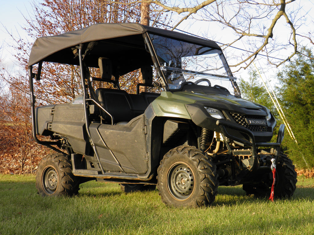 A Honda Pioneer 700-4 (2014+) with a soft top is parked on grass under warm sunlight, surrounded by bare trees and autumn leaves. The green utility vehicle features a black roof, winch, and off-road tires.