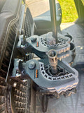 Close-up of an Offroad Armor Polaris Ranger Under Seat Hidden Rifle Mount securing a firearm inside a vehicle. The gray and black clamps attach to a rack, with the floor mat and seat visible in the background.