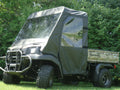 A Kawasaki Mule 3000/3010/4000/4010 with a Soft Full Enclosure and Vinyl Windshield sits on grass, featuring large tires and canvas sides, with dense green trees and bushes in the background.