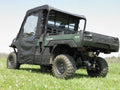 A Kawasaki Mule Pro-Fx with Soft Doors, Rear Window, and Top Combo for an existing hard windshield is parked on grassy terrain with small white flowers. It features rugged tires, a protective cab, and an open cargo bed under clear skies.