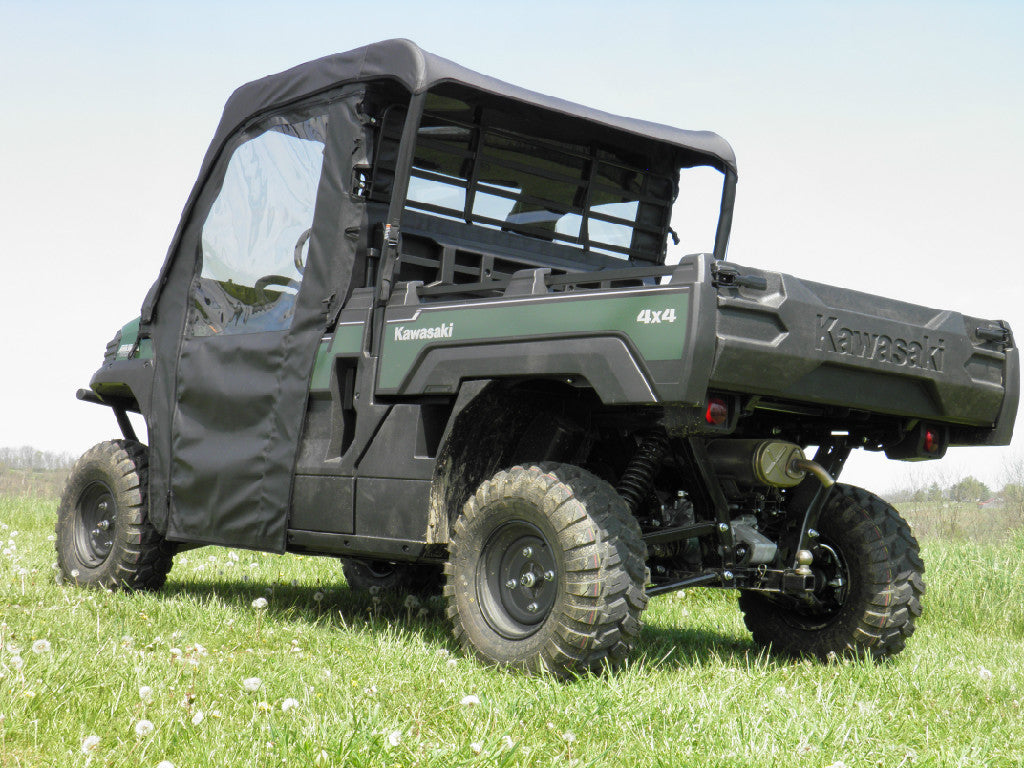 A Kawasaki Mule Pro-Fx with Soft Doors, Rear Window, and Top Combo for an existing hard windshield is parked on grassy terrain with small white flowers. It features rugged tires, a protective cab, and an open cargo bed under clear skies.