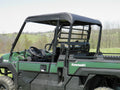 A Kawasaki Mule Pro-Fx Soft Top in green, featuring an open cab, black roof, and roll bars, is parked on grass with visible steering wheel and seats. Rolling hills, trees, and a clear sky provide a rural backdrop.