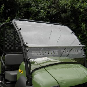 A Kawasaki Mule 600/610/SX Split Lexan Windshield with metal fasteners and center vents is mounted on a green utility vehicle with black trim, two gray seats, and dense green foliage in the background.