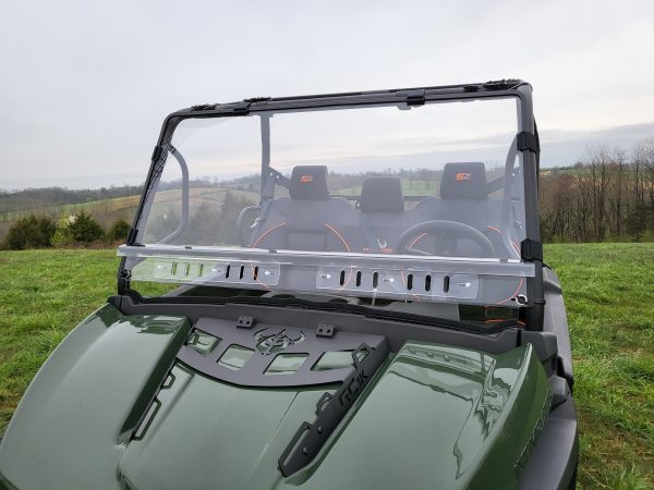 An Intimidator with a 2 Pc Windshield (optional vents, clamps, hard coat) features a clear windshield, two black seats with orange-accented headrests, and is parked on grassy hills under a cloudy sky. Photo taken from the front shows the hood.