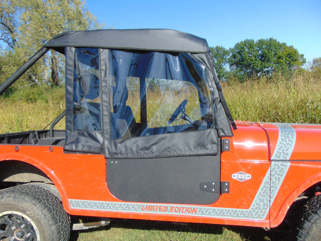 A close-up of a bright orange off-road Mahindra Roxor with “LIMITED EDITION” and “ROXOR” labels, featuring Upper Soft Doors with clear windows and a black soft-top, set against green grass, trees, and a blue sky.