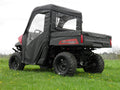 A Polaris Ranger with a Soft Full Cab Enclosure for an existing hard windshield is parked on grass, featuring clear windows and a cargo bed. The black utility vehicle is viewed from the rear passenger side on a cloudy day.