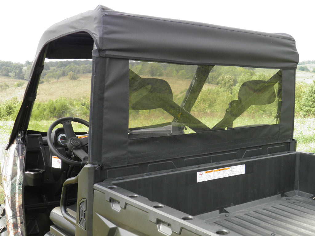 A Polaris Ranger Full and Mid-Size Soft Rear Window for all single cab models, featuring black fabric and a clear plastic window, is installed on a utility vehicle parked in an empty field with trees under a cloudy sky.