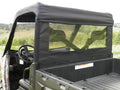 A Polaris Ranger Full and Mid-Size Soft Rear Window for all single cab models, featuring black fabric and a clear plastic window, is installed on a utility vehicle parked in an empty field with trees under a cloudy sky.