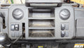 A close-up of a dusty vehicle dashboard, featuring two round air vents, three empty center compartments, several side switches, and a visible black cable—equipped with the John Deere 835/865 XUV Cab Heater with Defrost (2018-2024), Ice Crusher Cab Heater.