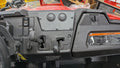 Close-up of a Honda Pioneer 700 (2023-2024) dash with the Ice Crusher Cab Heater installed, showing 2WD/4WD mode levers, switches, blank covers, a warning label on the right, and textured black plastic with some red body visible.