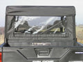 A Polaris Ranger Crew with a soft black fabric cab enclosure and a clear plastic rear window (Back Panel for all models). The empty cargo bed holds a small object near the cab. The vehicle sits on open grassy terrain beneath cloudy skies.