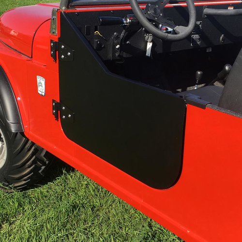 Close-up side view of a red off-road vehicle featuring Mahindra Roxor Premium Doors in matte black half-door style, revealing part of the black steering wheel, dashboard, and keys in the ignition; parked on green grass.