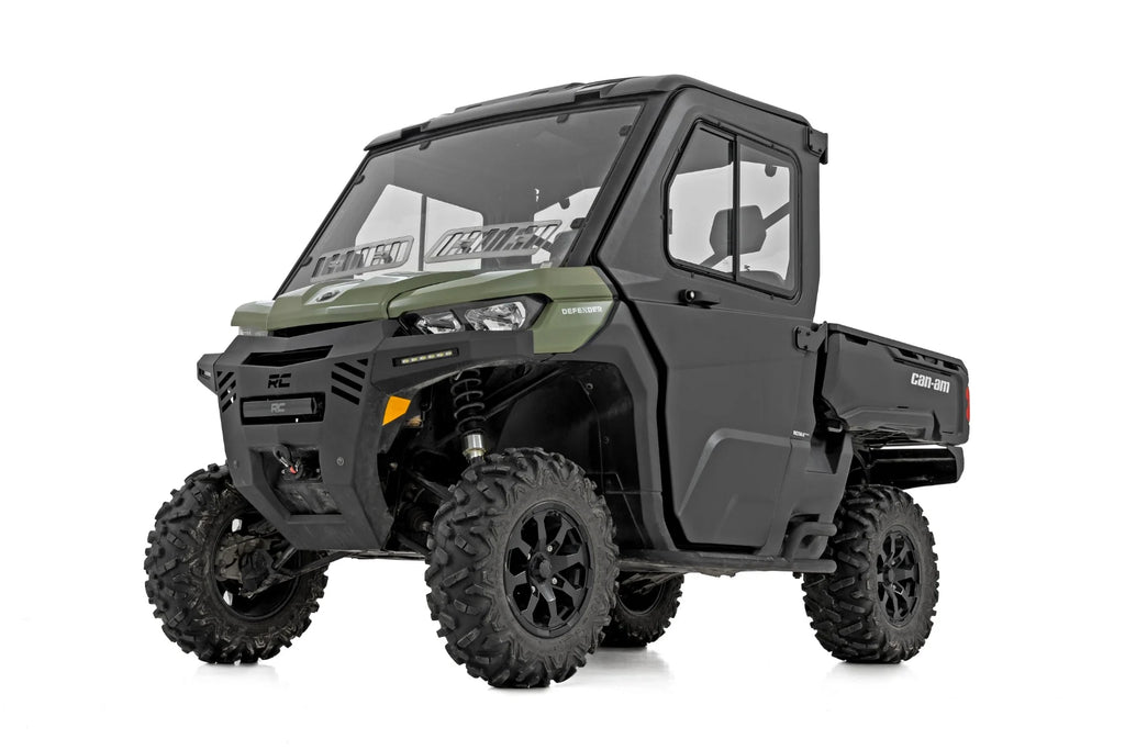 A green and black 2 Seater Can-Am Defender HD 5/HD 7/HD 8/HD 9/HD 10 with doors, large knobby tires, enclosed cabin, windshield, cargo bed, and side doors is shown front-side view on a white background.