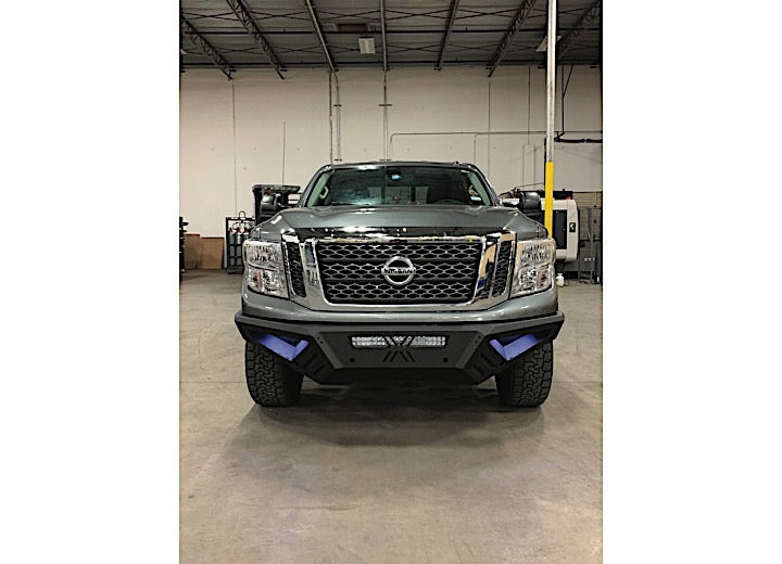 A gray Nissan pickup with a 2016-2019 Titan XD Spartan Front Bumper in textured black, featuring LED lights and rugged tires, is parked indoors in a spacious warehouse with high ceilings.