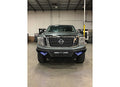 A gray Nissan pickup with a 2016-2019 Titan XD Spartan Front Bumper in textured black, featuring LED lights and rugged tires, is parked indoors in a spacious warehouse with high ceilings.