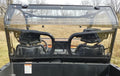 View from the cargo bed of a CFMoto UForce 500/800 equipped with a 2-piece Lexan Back Panel (includes soft lower panel with clamp and vent options), looking through the rear windshield at two black bucket seats; grassy field and overcast sky in the backgr