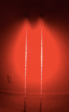 Two Woodys Whips 4FT LED light strips, placed parallel and close together, emit a vivid red glow that fills the area. An electrical outlet appears on the lower left side of the wall.