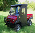 A 2013-2021 Kawasaki Mule® 4010 (2 Seat) with large tires, a closed cab, fixed windshield, side windows, and a red cargo bed is parked on green grass with trees and sunlight in the background.
