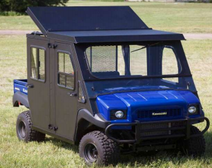 A 2013-2021 Kawasaki Mule Trans with an insulated steel top and raising rear panel, featuring a black cab, mesh windows, front grill guard, large off-road tires, and boxy shape, is parked on grass with trees in the background.