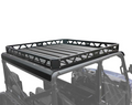A black Roof Rack Kit for Polaris Ranger Crew XP1000 (2018-2021) with a flat, slatted base and raised sides is mounted on an off-road vehicle with an open cabin. The roof rack stands out against the white background.