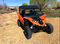 A Yamaha side-by-side with large tires, black roof, and a 2016-2017 Yamaha Yxz Full Front Glass Windshield With D.O.T Stamp is parked on gravel. Trees, fields, a fence, and buildings are visible under a blue sky.