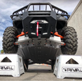 Low-angle view of a Polaris Ranger 1000 lifted on two white “Rival” branded ramps, showing the suspension and orange Alloy Central Skid Plate undercarriage against a cloudy sky and concrete wall.