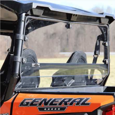 A close-up of the rear side of an orange off-road vehicle with GENERAL written on it, featuring two black seats and a Seizmik Rear Windshield. The clear windshield shows a blurred outdoor scene with grass and trees in the background.