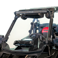 A close-up of a 2018+ Polaris RS1 Versa-Vent Hard Coated Front Windshield shows a black off-road vehicle with an LED light bar on top, plus a red-accented seat, steering wheel, and angular modern dashboard details inside.